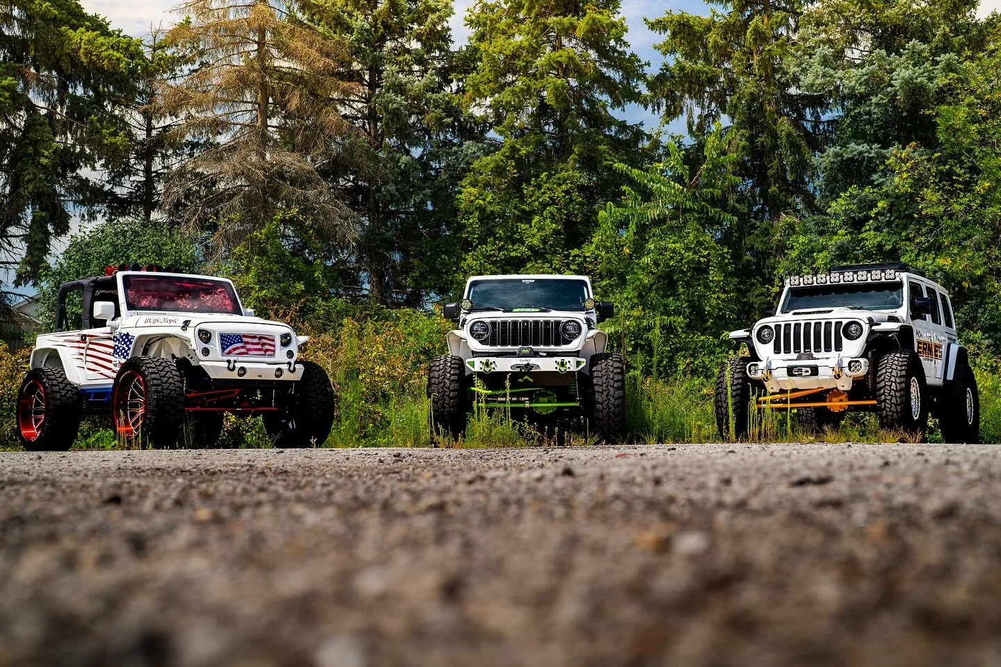 Three Jeep Wranglers built by Ernie's Custom Shop, lined up on a gravel road